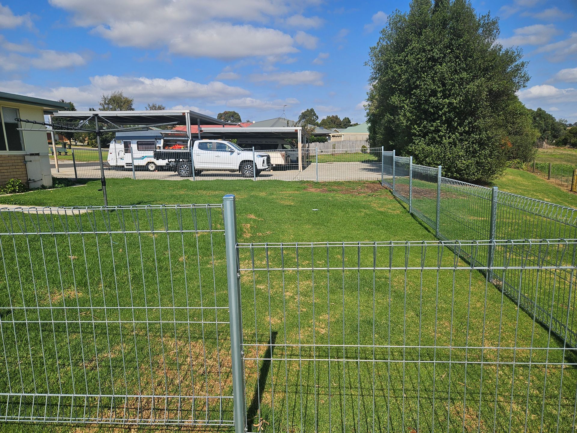 A white truck is parked in a grassy field behind a fence.