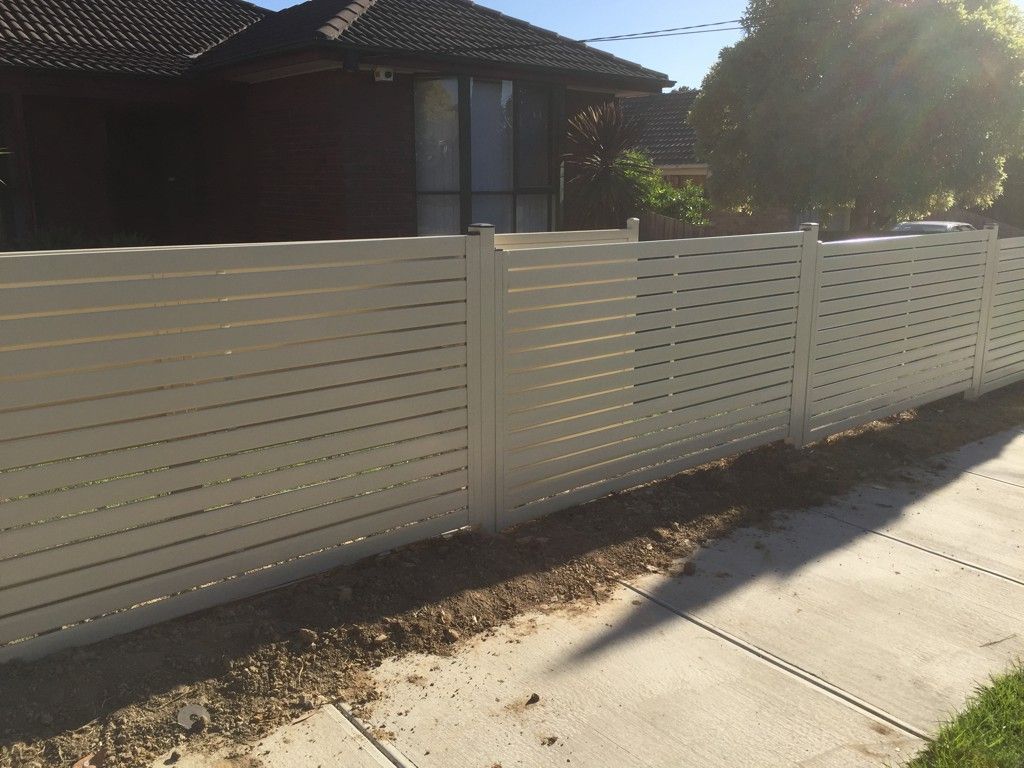 A white fence along a sidewalk in front of a house