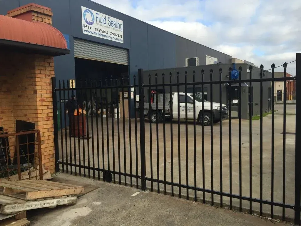 A white truck is parked in front of a building behind a black fence.