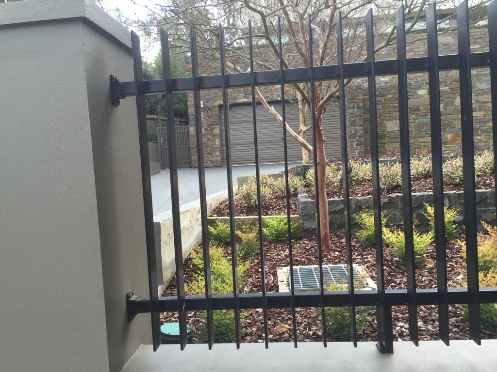A black metal fence surrounds a lush green garden