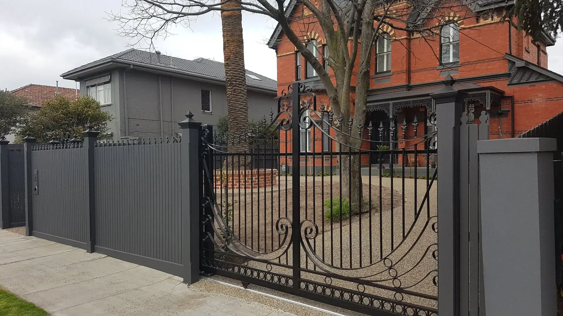 A large brick house is behind a fence with a sliding gate.