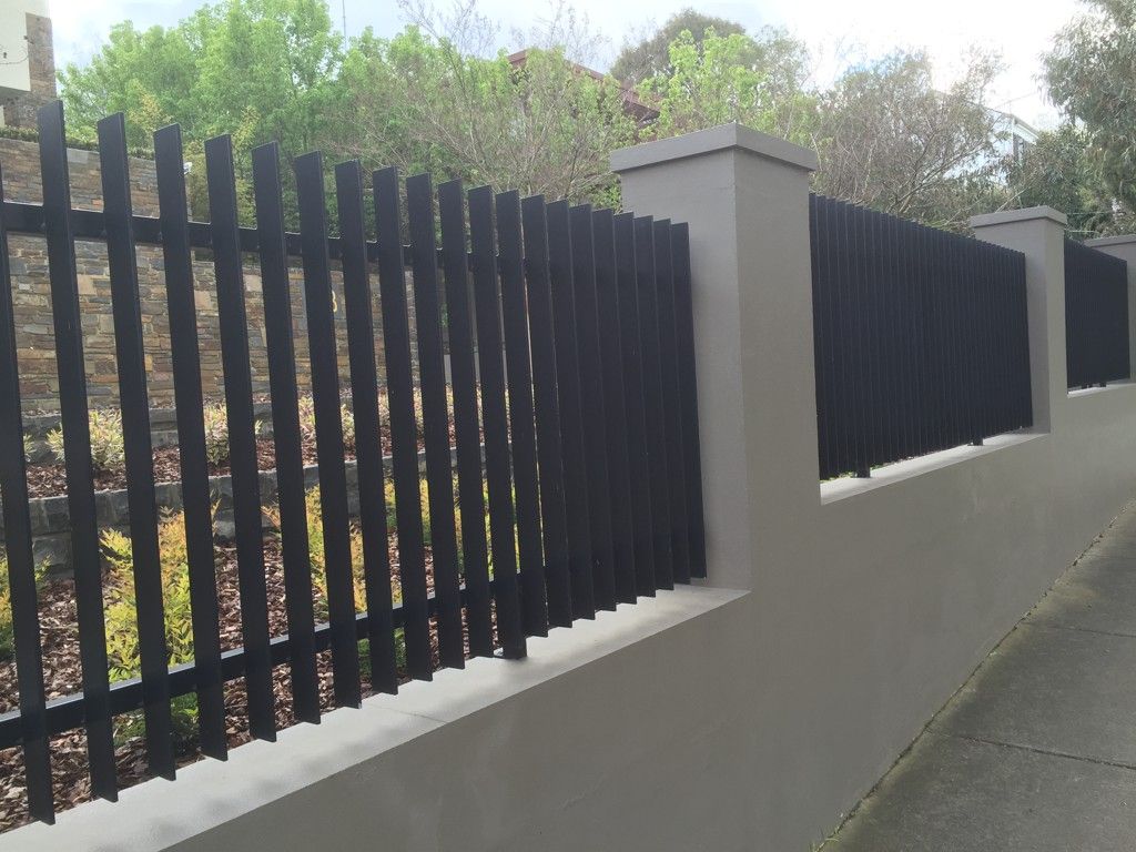 A black fence with a white wall behind it