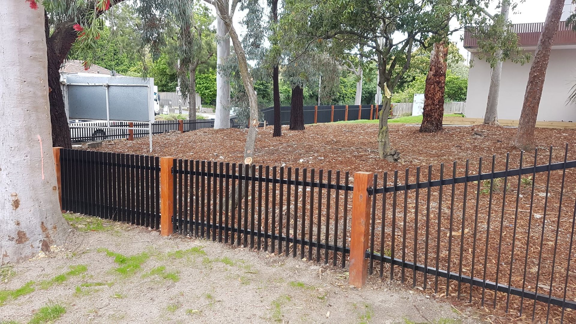 A black fence with wooden posts is surrounded by trees and leaves.