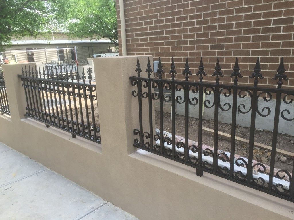A wrought iron fence with a brick wall in the background