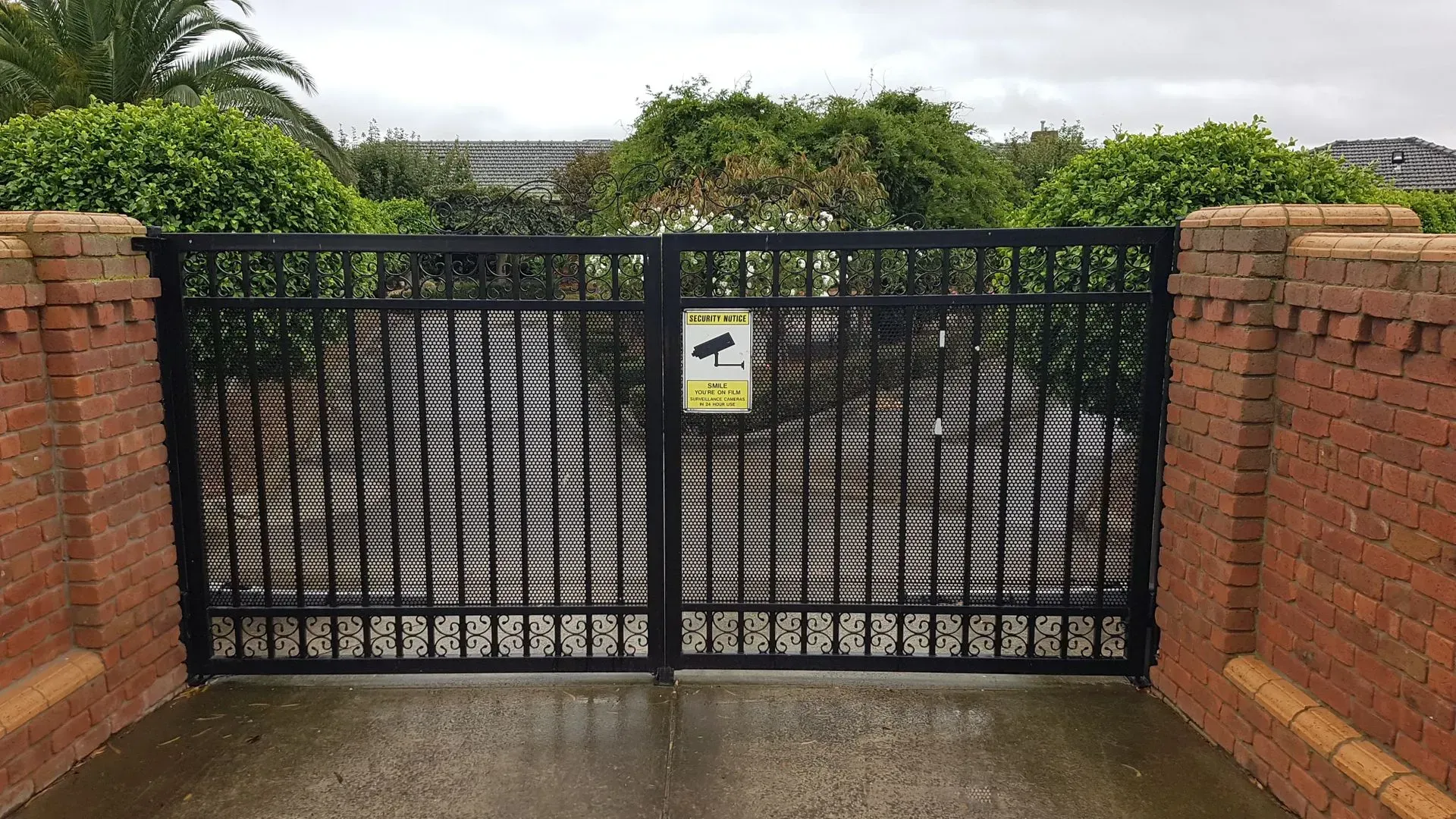 A black gate with a yellow sign on it is surrounded by a brick wall.
