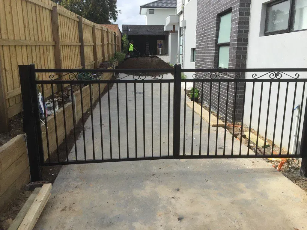 A black metal gate is open to a driveway in front of a house.
