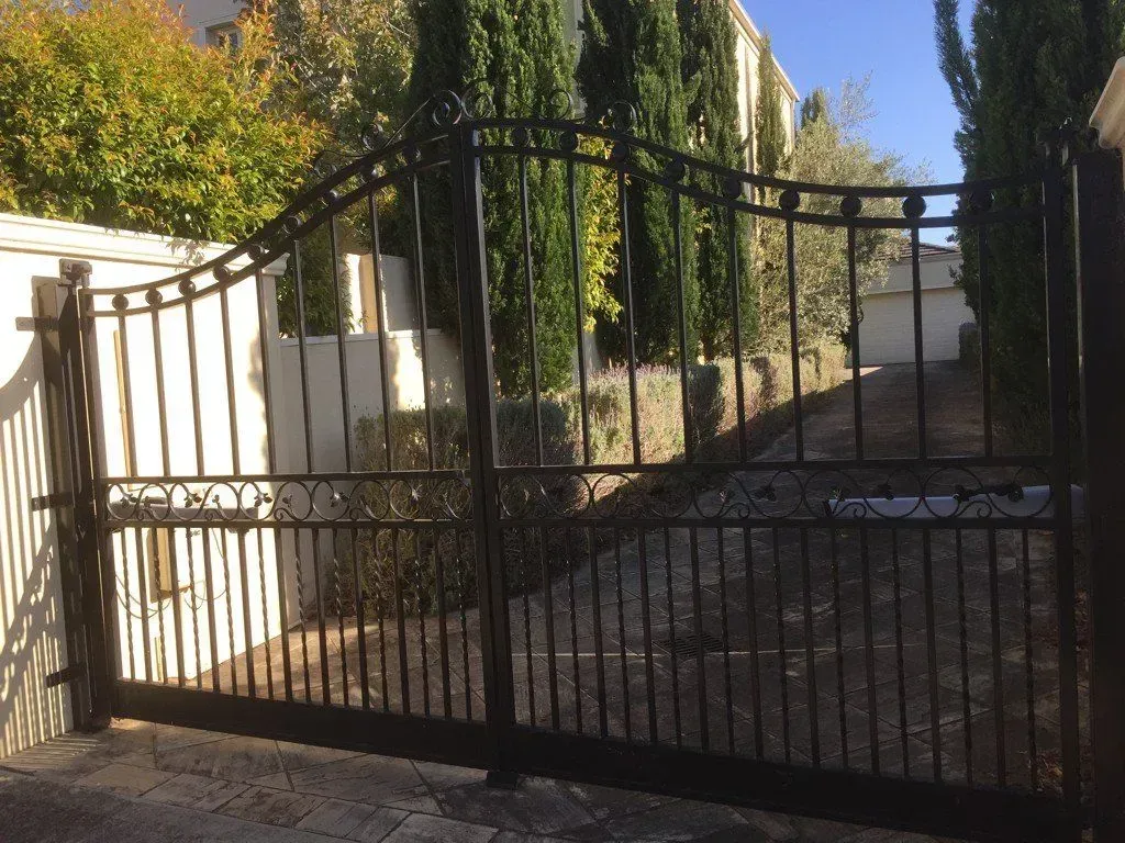A black wrought iron gate is open in front of a house.