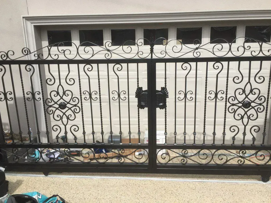 A wrought iron gate is sitting in front of a garage door.