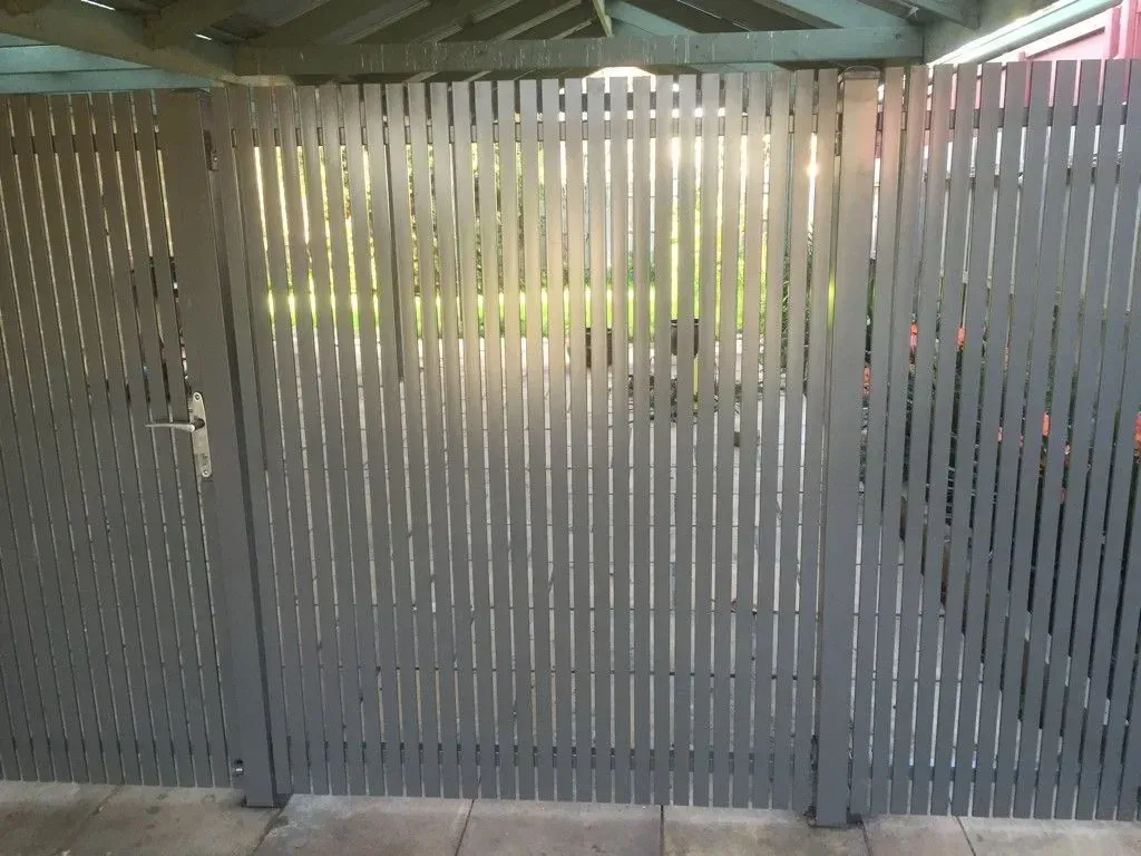 A fence with a door that is open and a car parked behind it