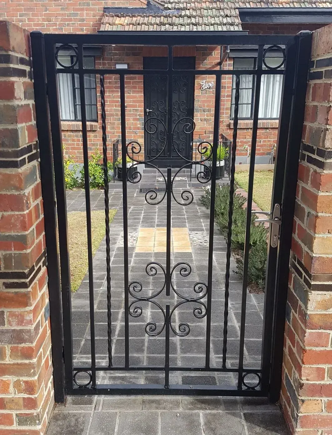 A black wrought iron gate is sitting in front of a brick building.