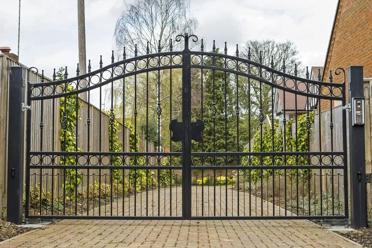 A black wrought iron gate is open to a driveway.