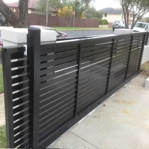 A black sliding gate is sitting next to a sidewalk.