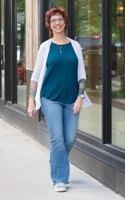 Licensed Professional Counselor walking on a Virginia Beach sidewalk, wearing a teal top, jeans, and a white cardigan.