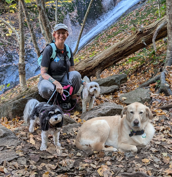Counselor hiking with three dogs on a forest trail beside a waterfall in Virginia