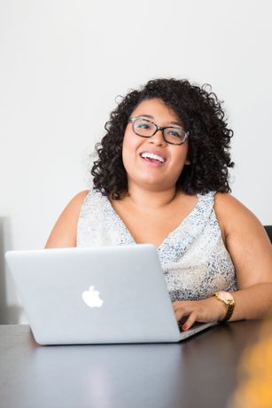 Smiling woman with curly hair and glasses using a laptop for teletherapy