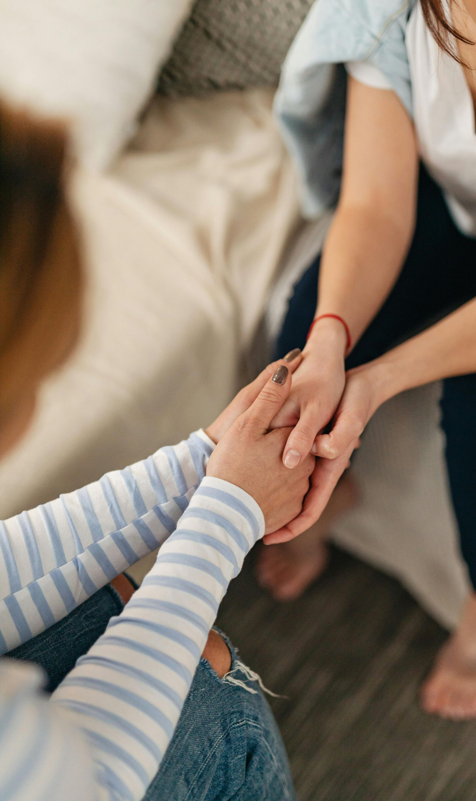 Two people holding hands in a cozy indoor setting, one wearing a striped sleeve and jeans.