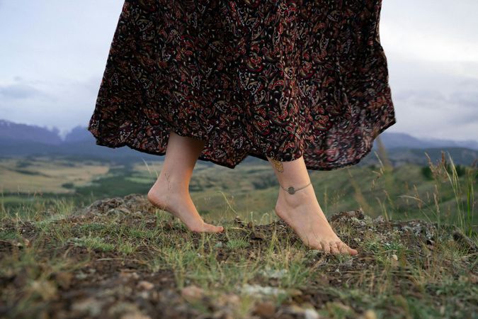 Bare feet grounding for therapy with a dark floral skirt and mountains in the background