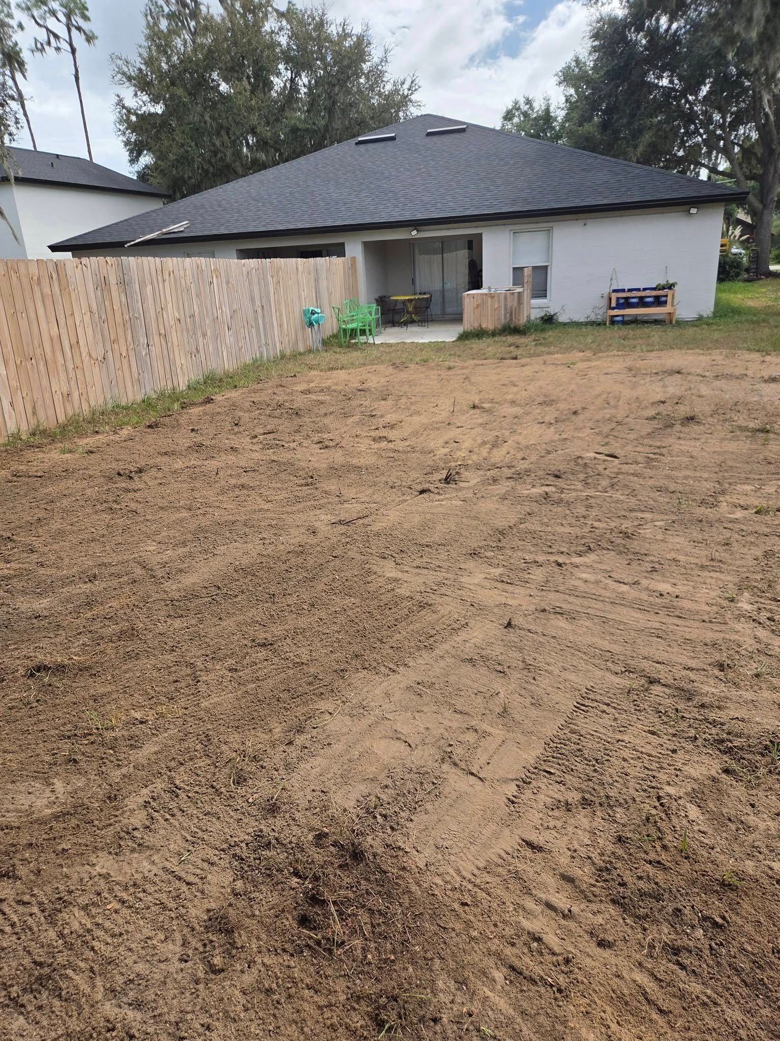 Backyard with bare soil, a house, and a wooden fence.