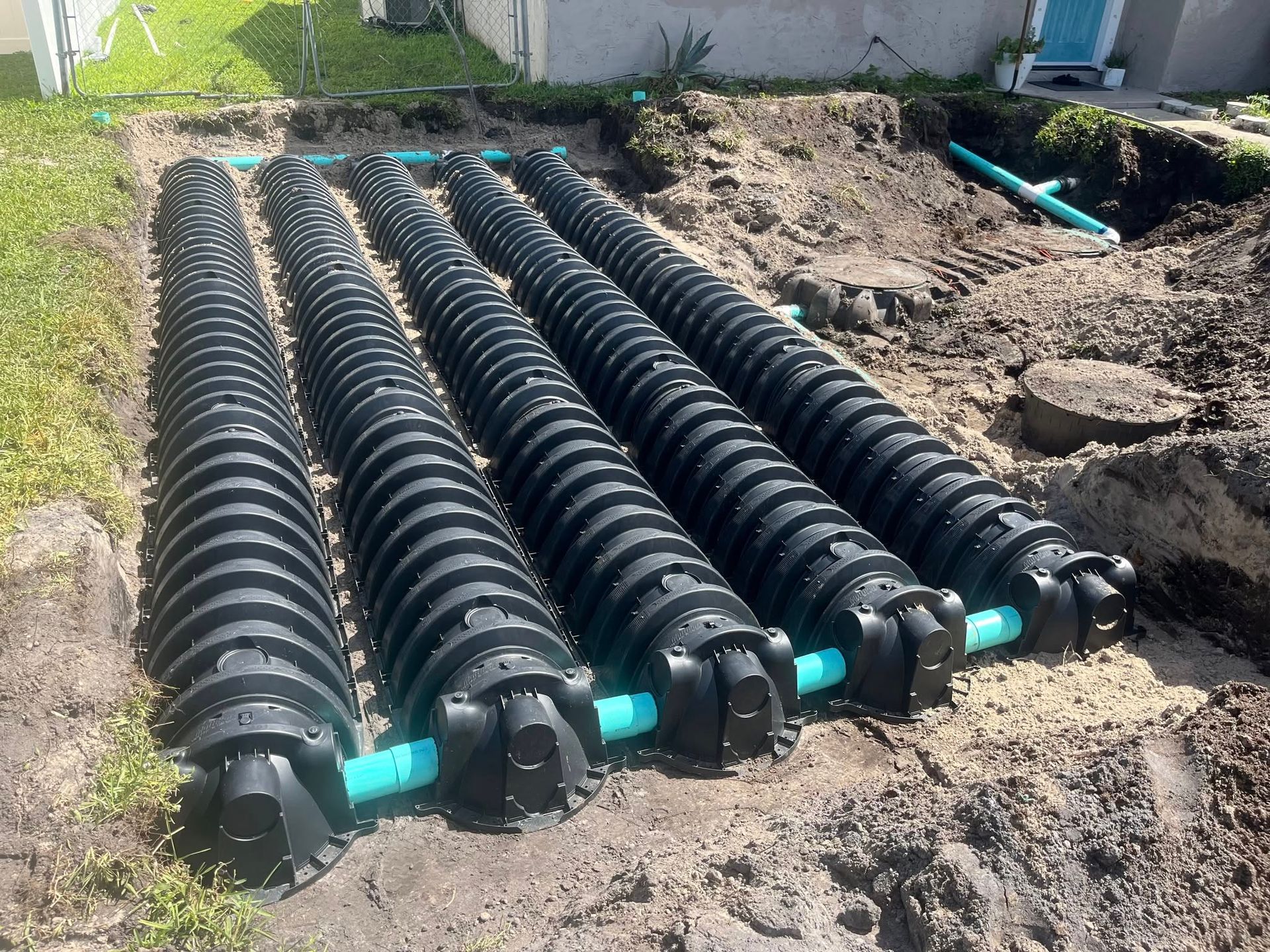 Four large black plastic septic tanks installed in a dirt trench, connected by green pipes.