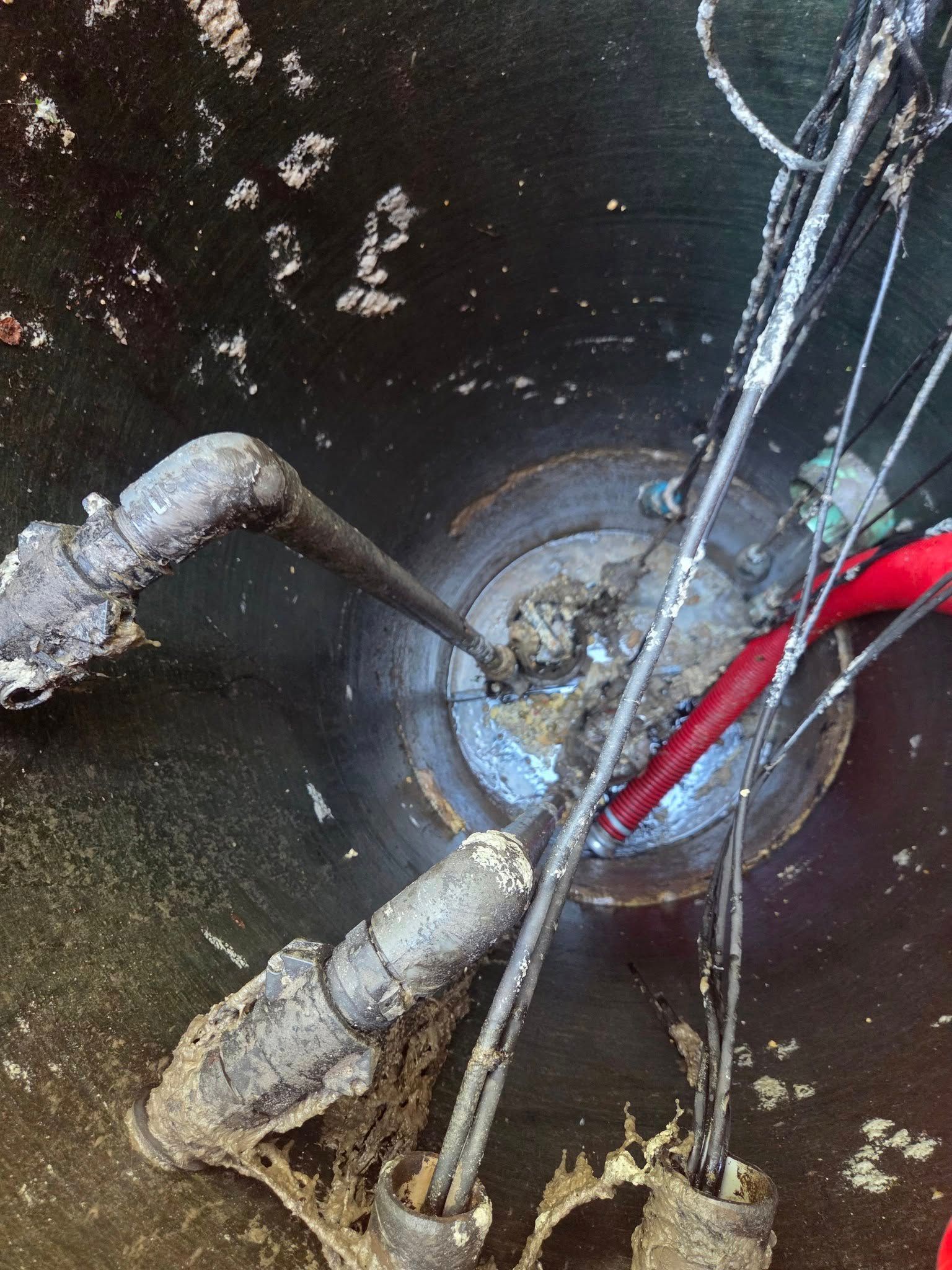 Overhead view of a dark metal tank opening with pipes and wires coated in a white substance.