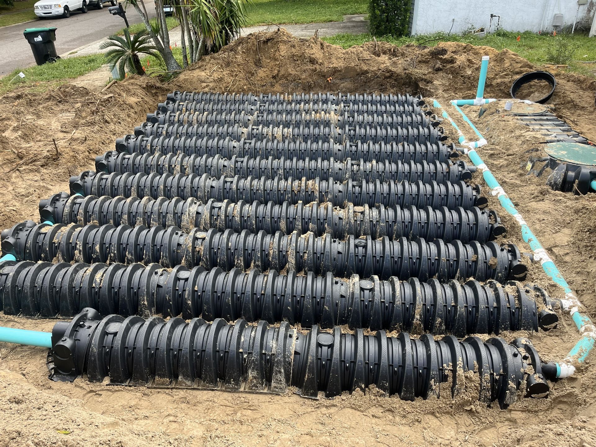 Black septic tank drain field laid in a dirt trench, connected by blue PVC pipes.