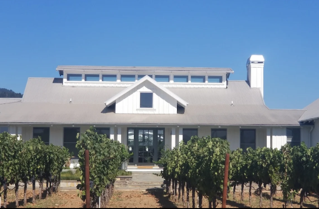 White winery building with vineyard in front, clear blue sky.