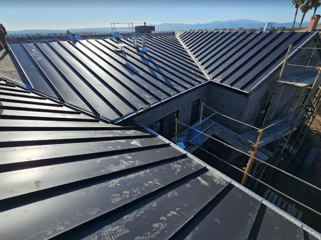 Black metal roof of a building under construction, with scaffolding visible on the side and a clear sky above.