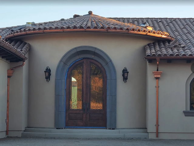 Tan stucco house with copper gutters and a rounded entryway with wooden double doors — Modern House Construction with Metal Roof in Napa, CA