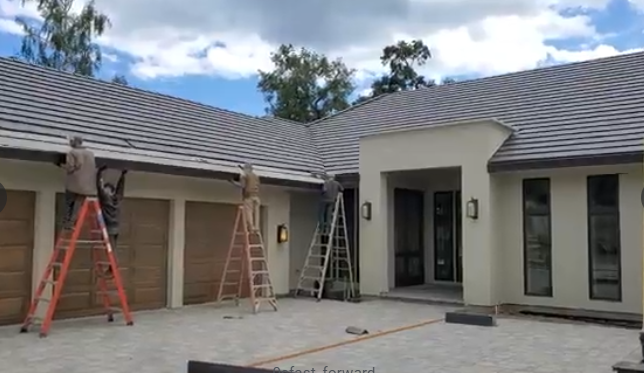 Workers installing gutters on a house with a tile roof; men on ladders.