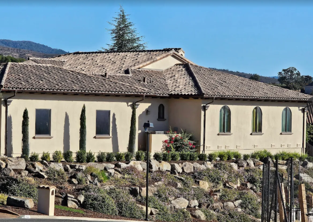 Beige stucco building with arched windows, tile roof, and landscaping on a hillside.