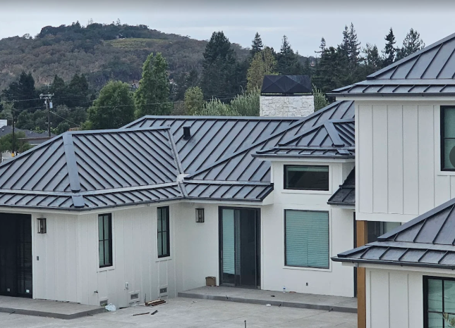 Modern home with a dark gray metal roof, white siding, and mountain backdrop.
