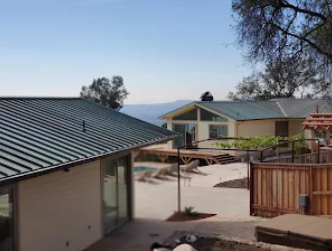 Two houses on a hillside with blue sky, one with green metal roof, a patio and view — Modern House Construction with Metal Roof in Napa, CA