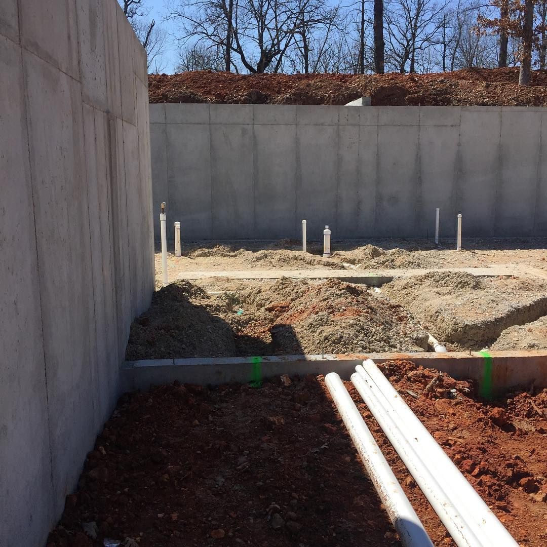 Construction site: concrete foundation walls, exposed plumbing pipes, and dirt.