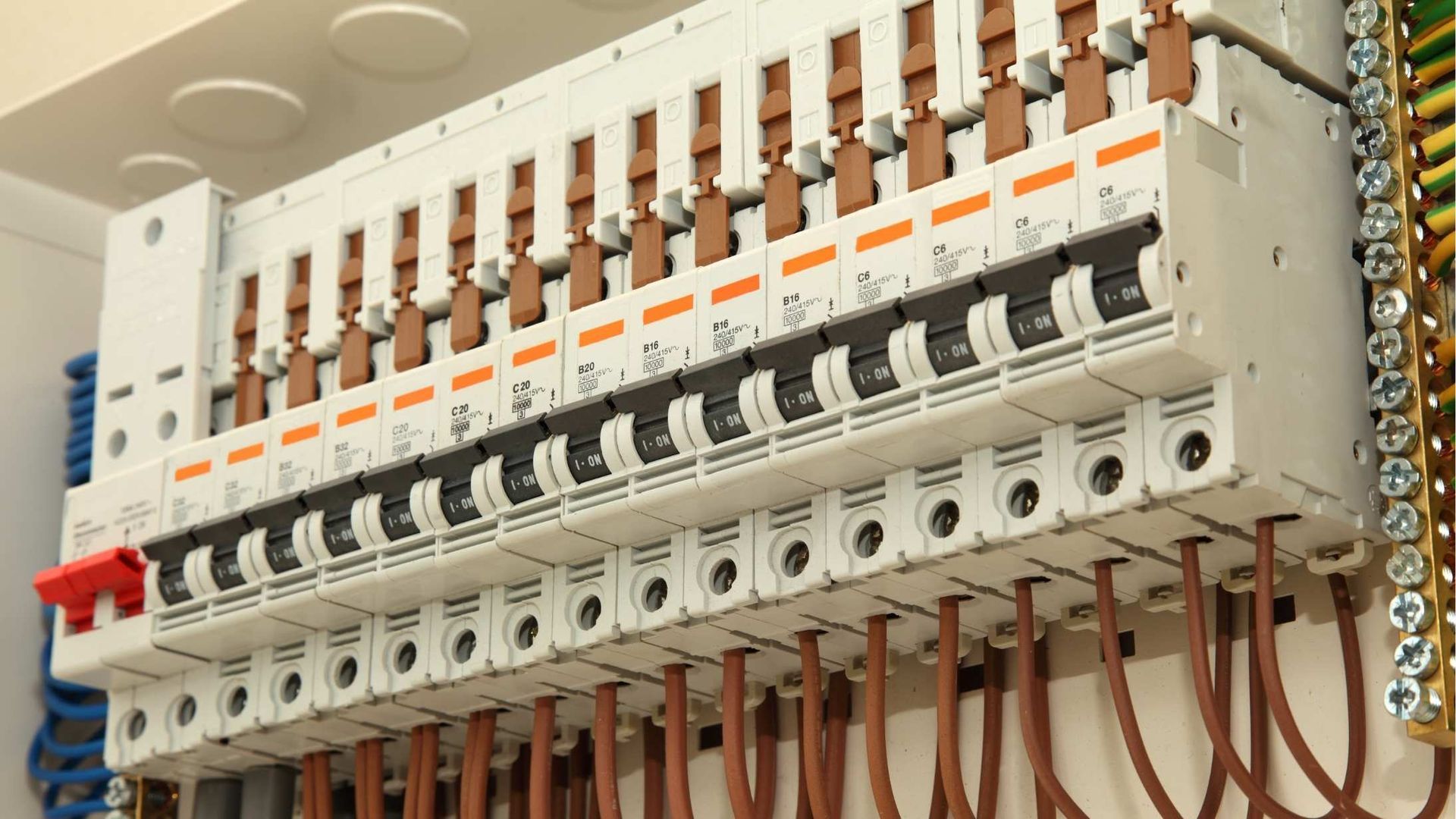 A close-up of an electrical panel with rows of circuit breakers and brown wires. The breakers are in the