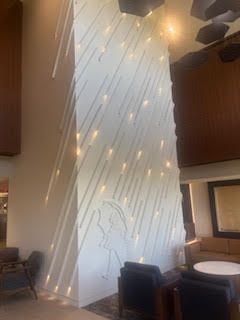 A tall white wall with embedded lights in a rain pattern, a person with an umbrella is etched.