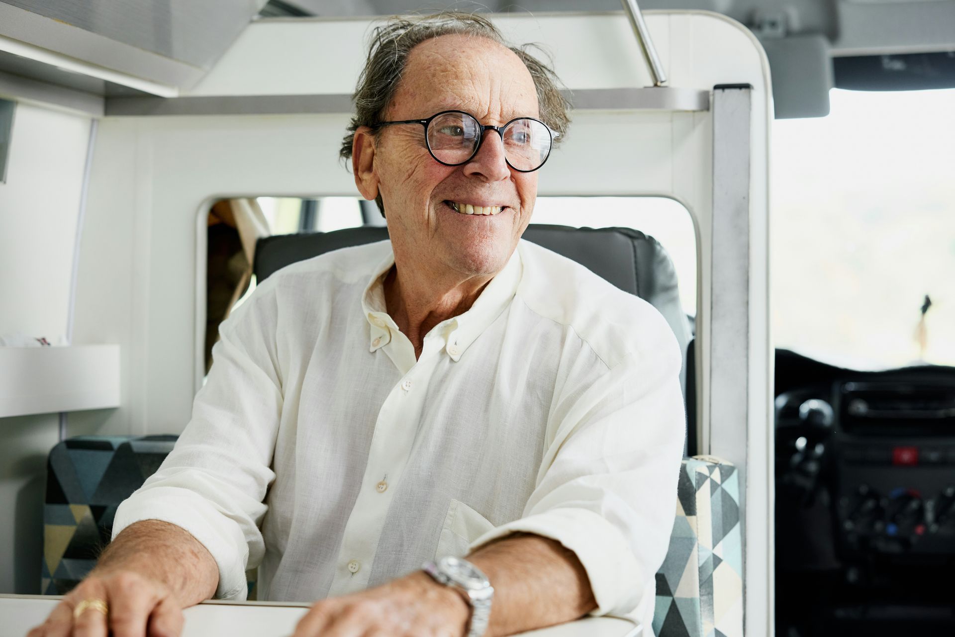 An older man wearing glasses is sitting in a camper van.