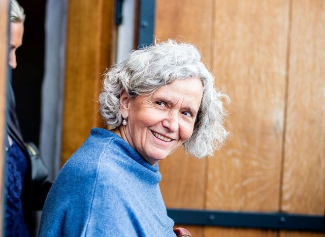 A woman with gray hair is wearing a blue sweater and smiling.