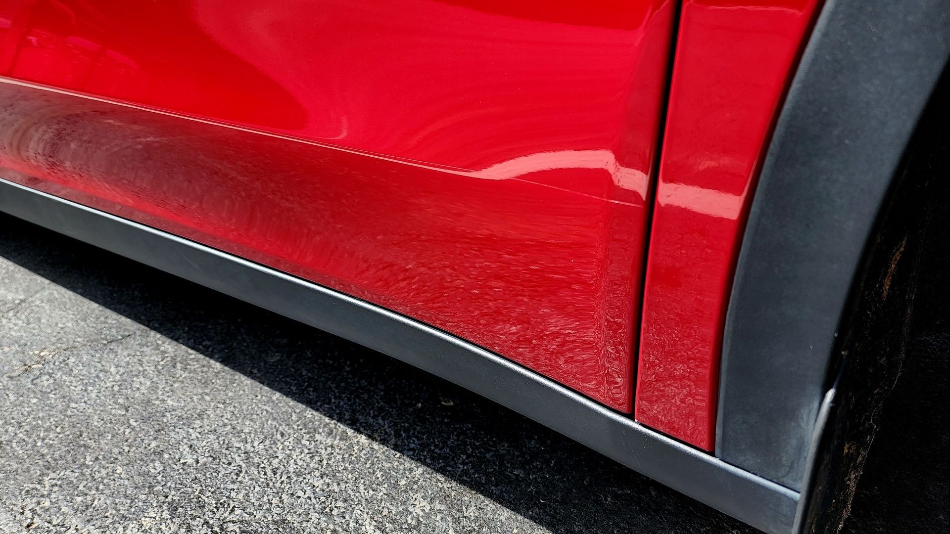 A red car with black trim is parked on the side of the road.