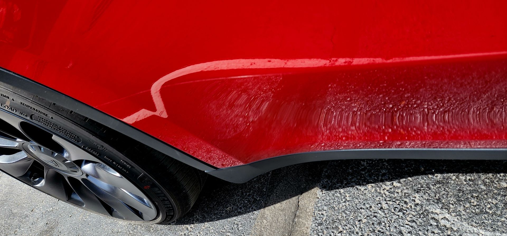 A close up of a red car with a scratch on the side.