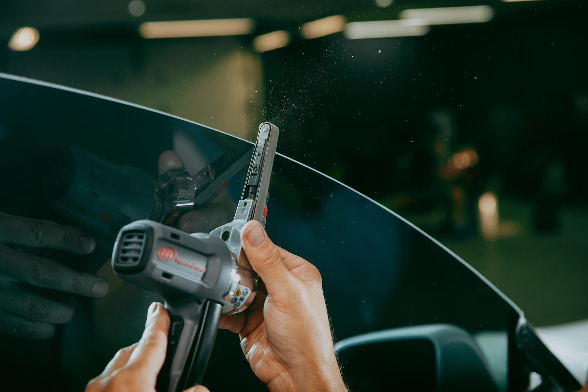 A person is holding a tool over a car windshield.