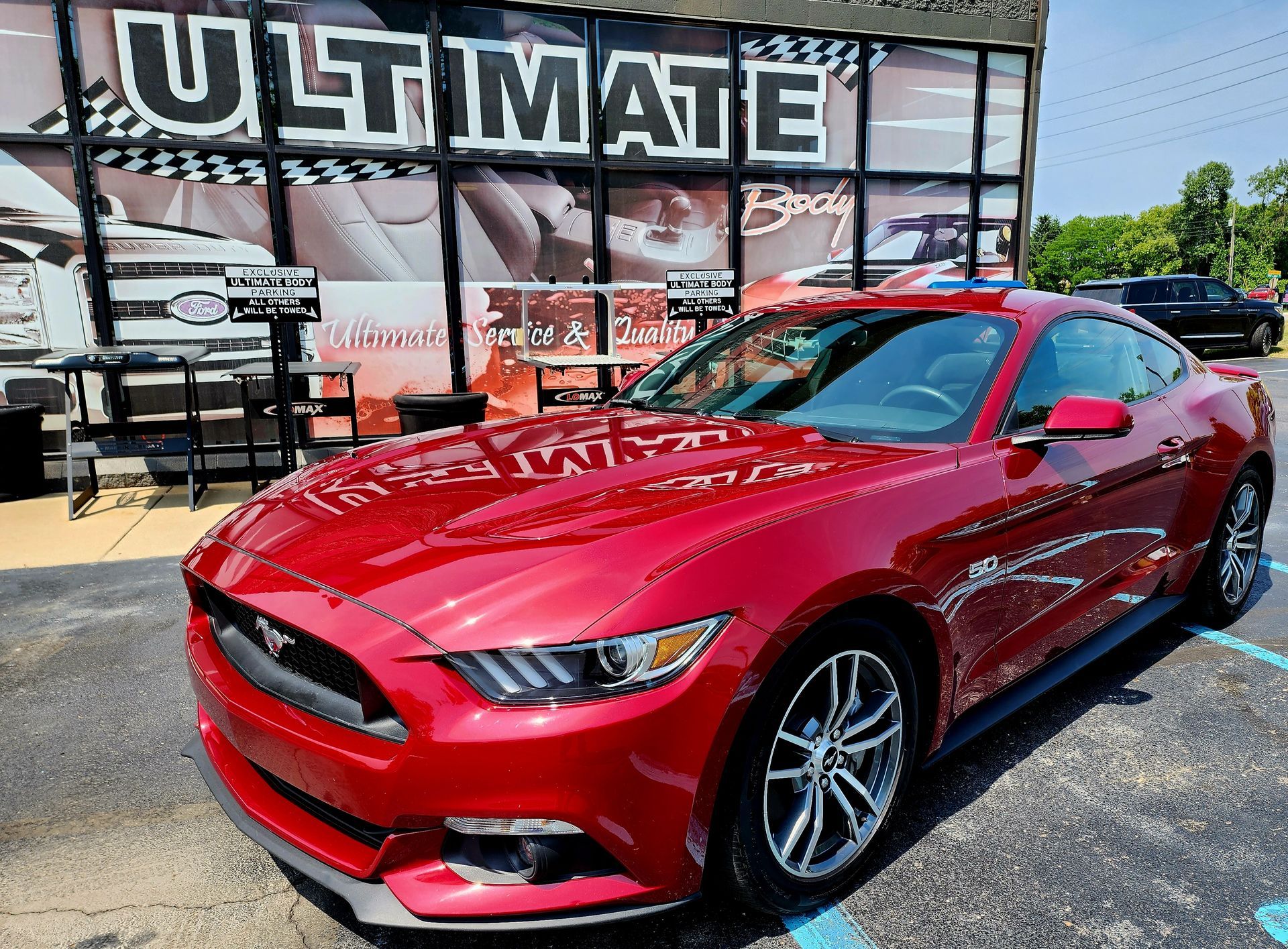 A red mustang is parked in front of a building that says ultimate