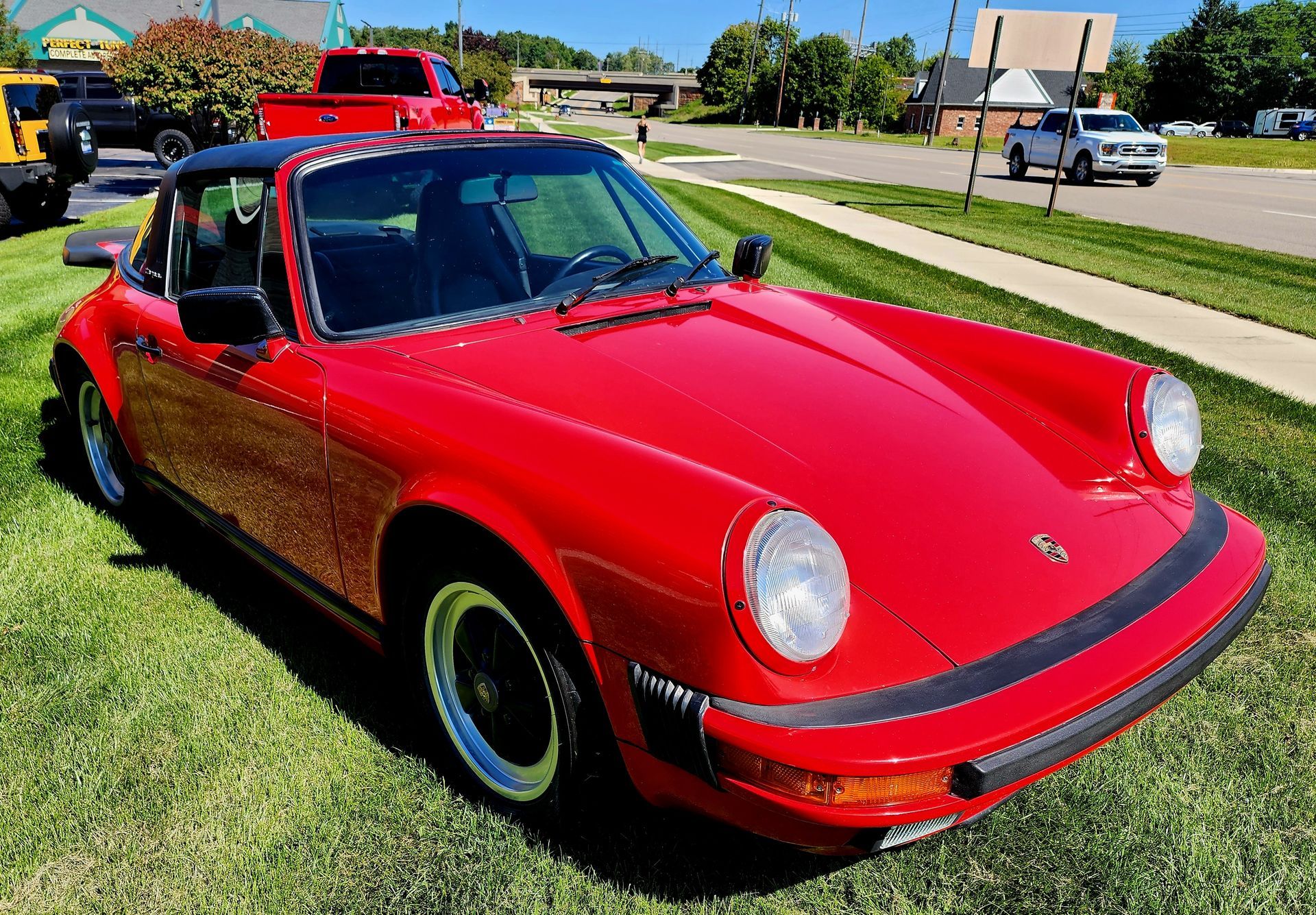 A red porsche targa is parked on the grass in a parking lot.
