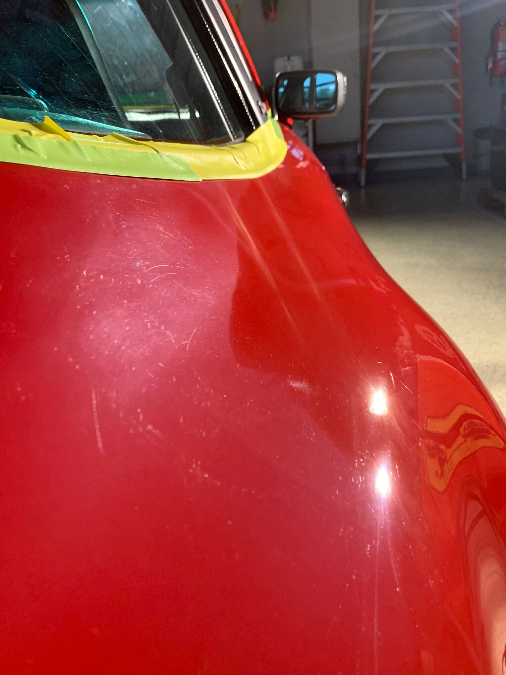 A close up of a red car with yellow tape on the hood