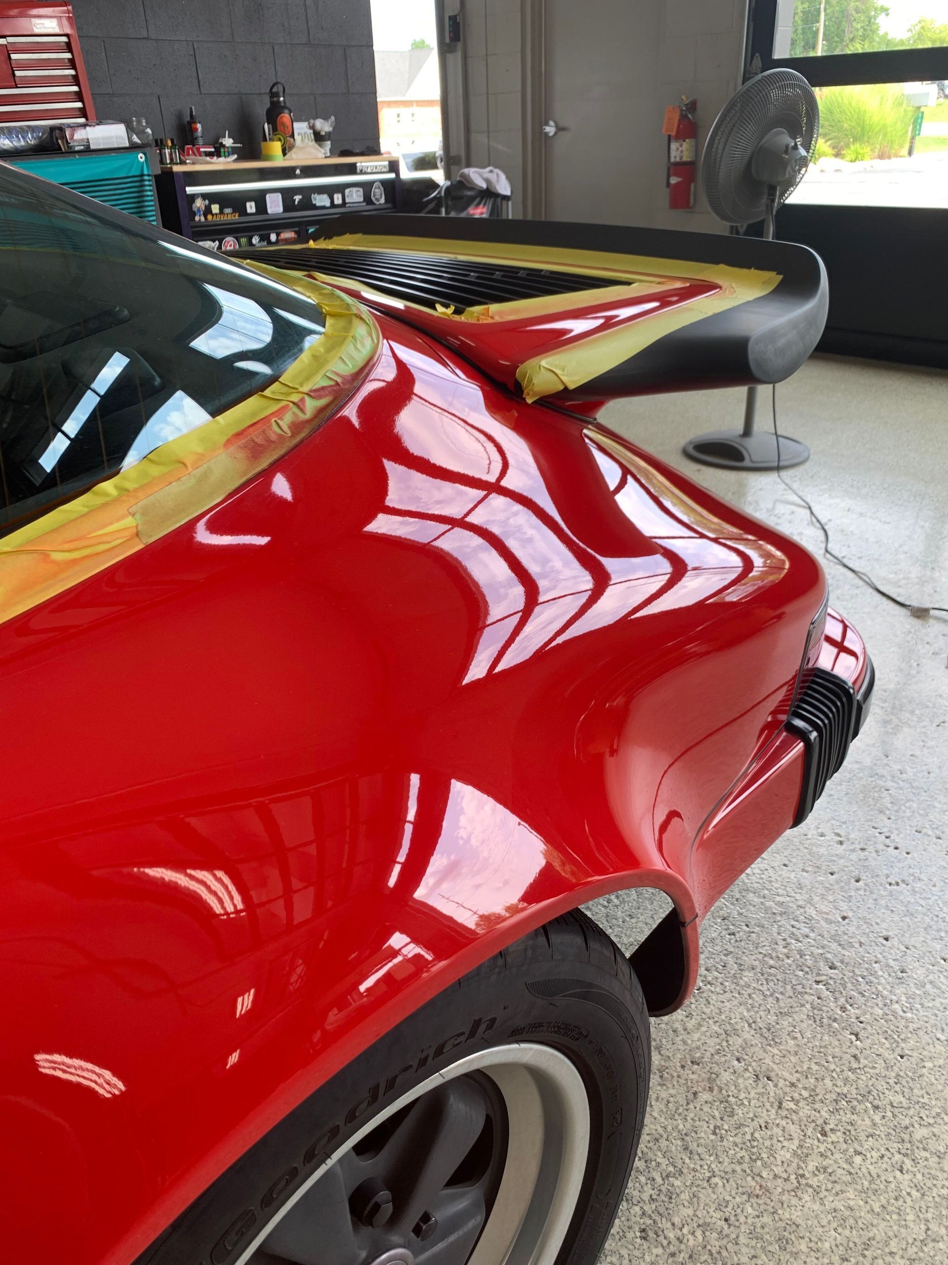 A red car is sitting in a garage next to a fan