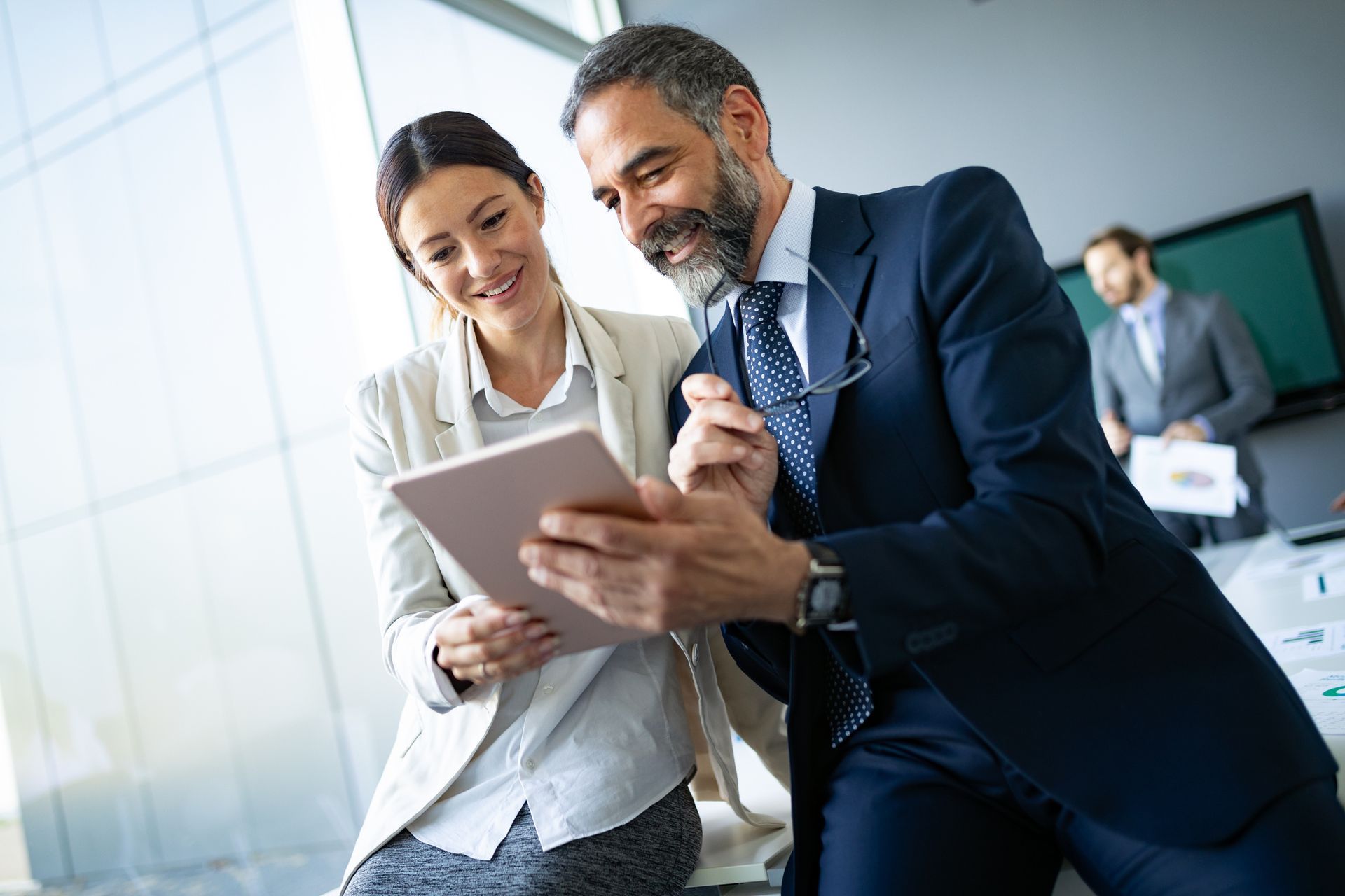 A man and a woman are looking at a tablet in an office.