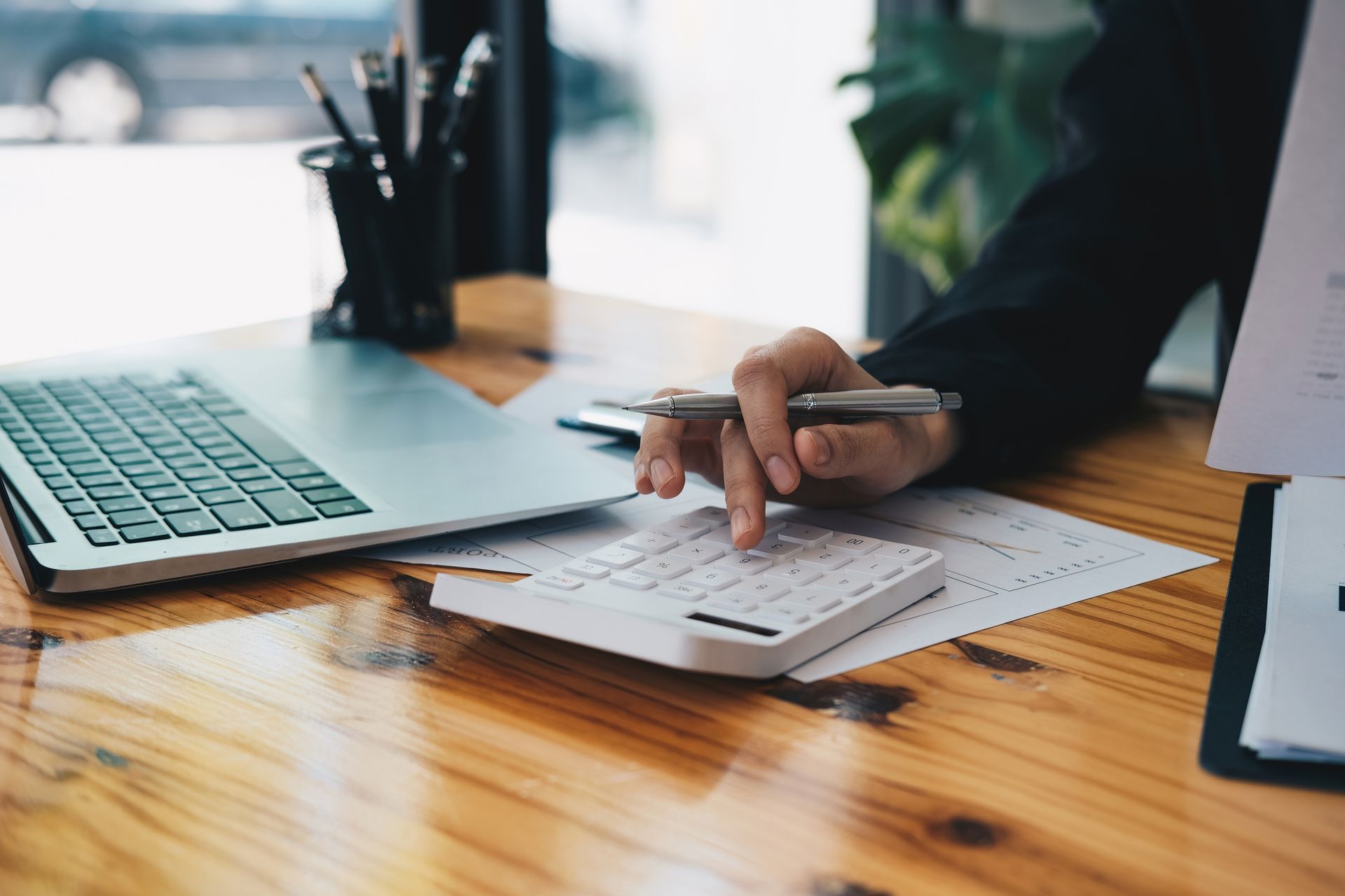 A person is sitting at a desk using a calculator and a laptop.