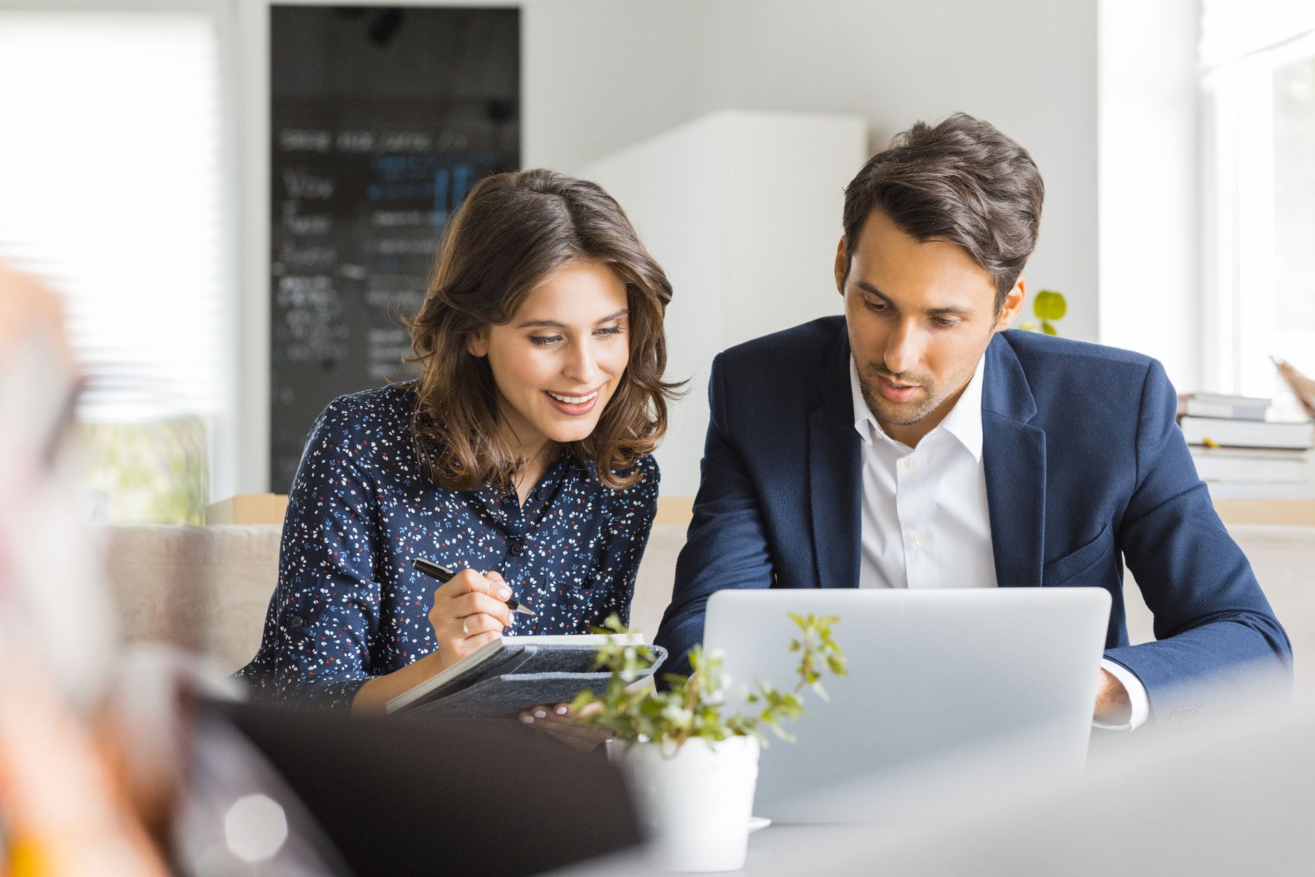 A man and a woman are sitting at a table looking at a laptop.