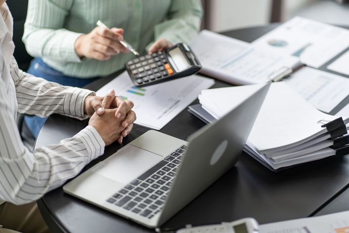 Two people are sitting at a table with a laptop and a calculator.