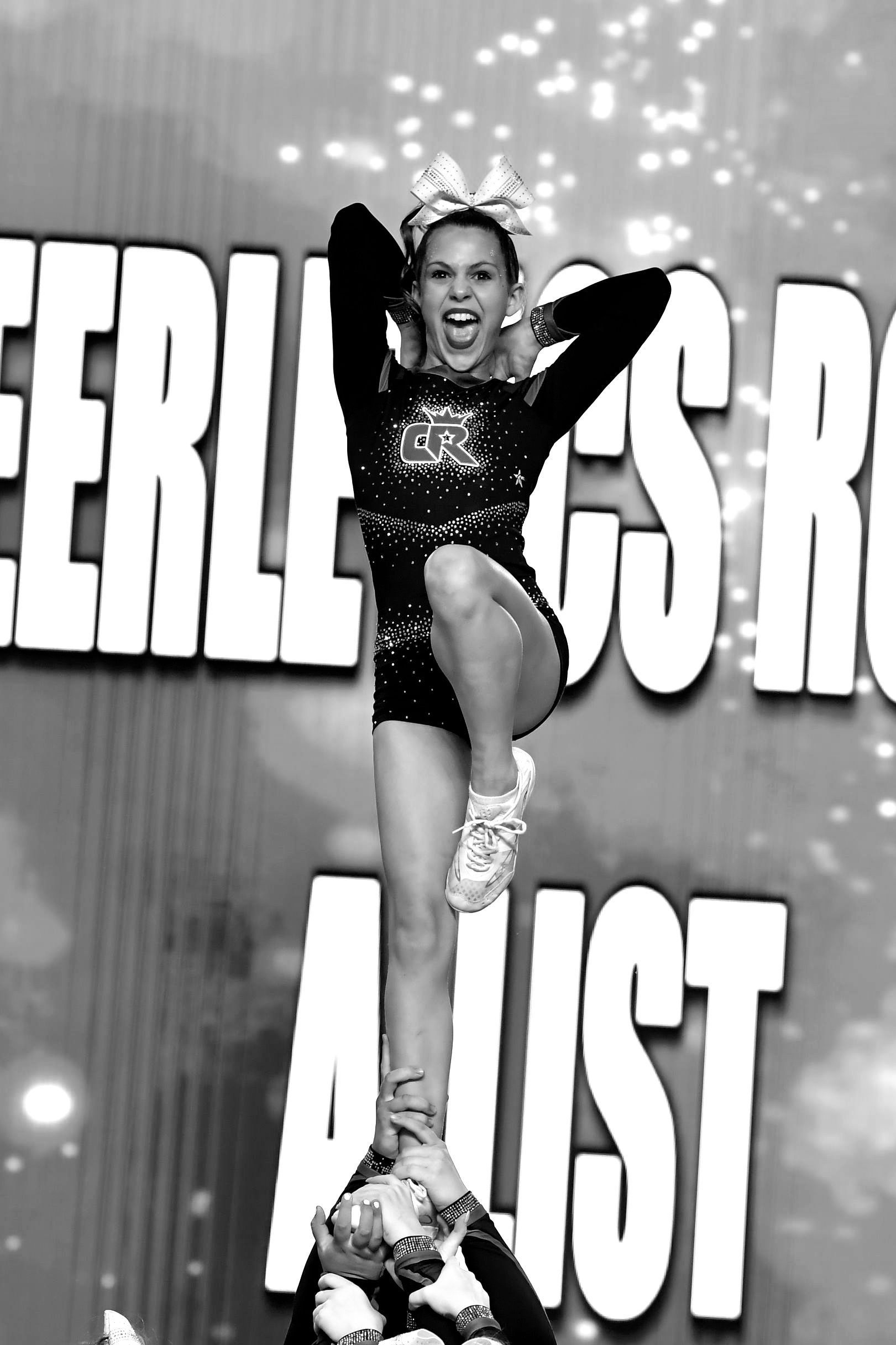 A cheerleader is doing a trick in front of a sign that says cheerless adjust