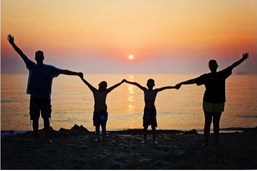 Life Insurance Policies - A family holding hands standing Infront of the ocean with a sunset